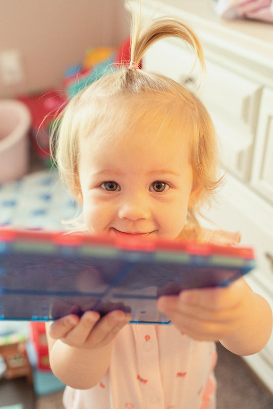 A smiling toddler holds a toy in a room.