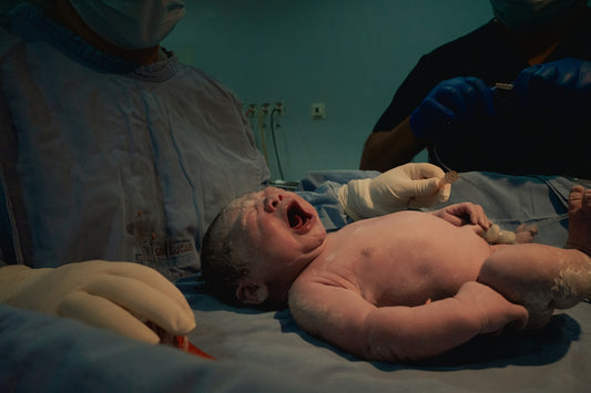 Newborn baby crying during childbirth with medical staff.