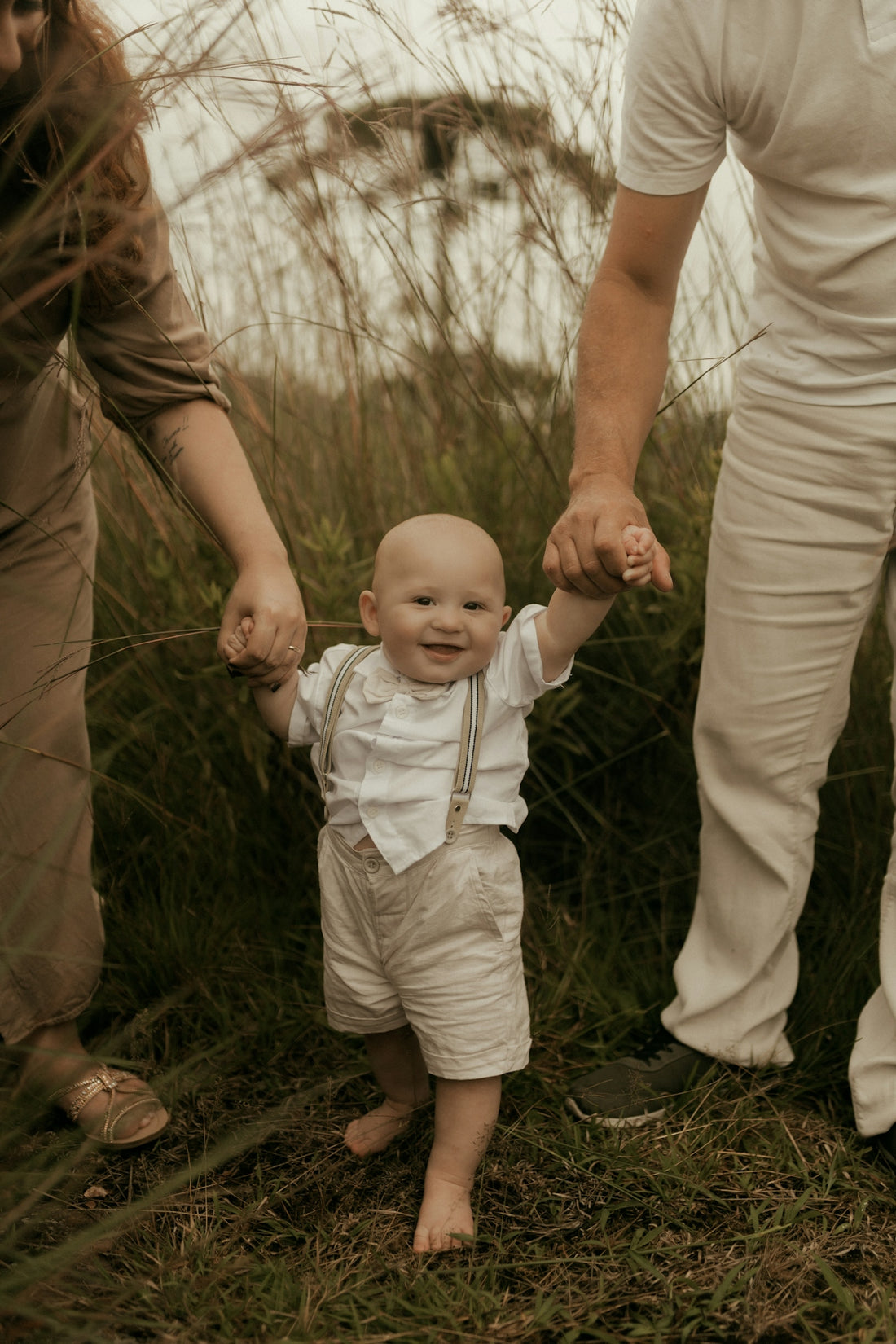 Parents holding hands with happy baby walking in grass